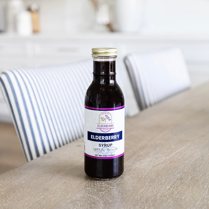 Bottle of elderberry syrup surrounded by fresh elderberries and leaves on a rustic wooden background.
